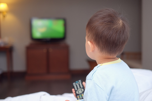 Un enfant face à une télévision et la télécommande à la main.