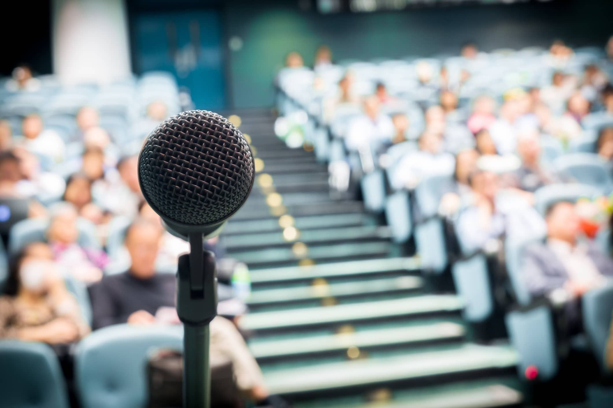 Image d'illustration représentant un micro ouvert face à un public dans une salle de conférence.