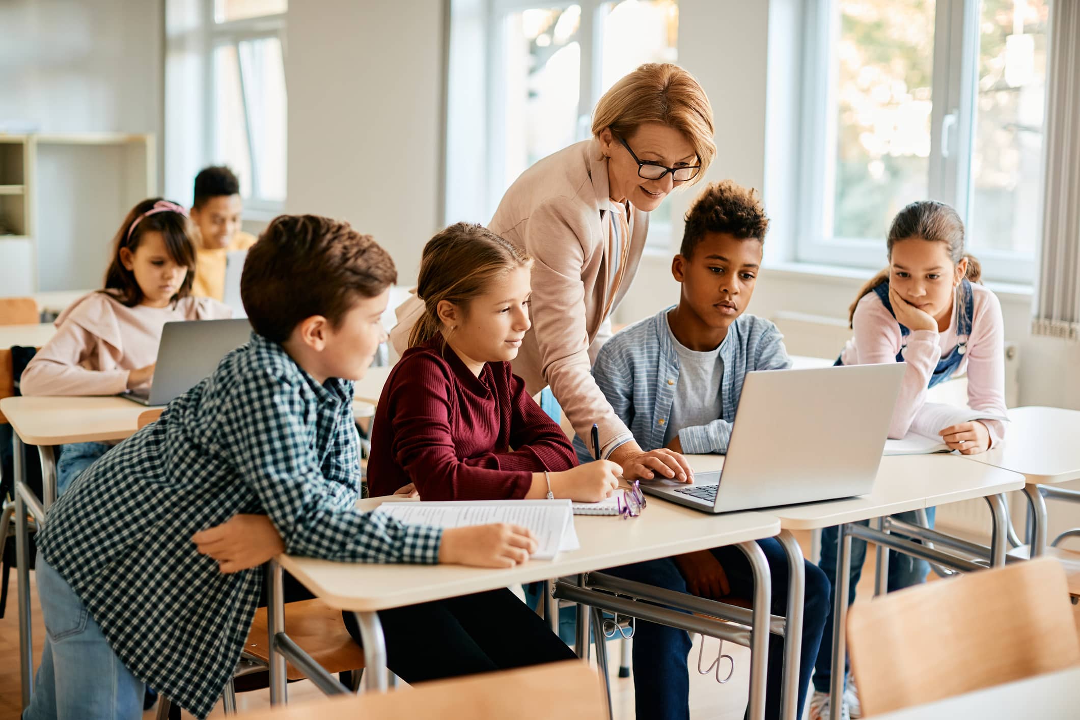 Une professeure entourée de ses élèves devant un ordinateur portable.