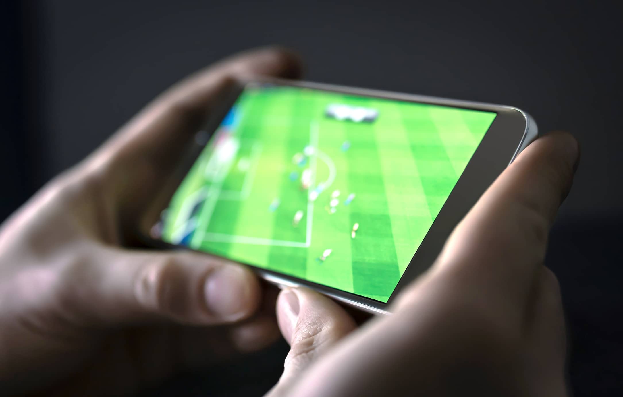 Image d'une personne tenant dans ses mains un smartphone sur lequel est diffusé un match de football.